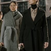 A group of fashionable women in coats standing confidently in an urban environment.