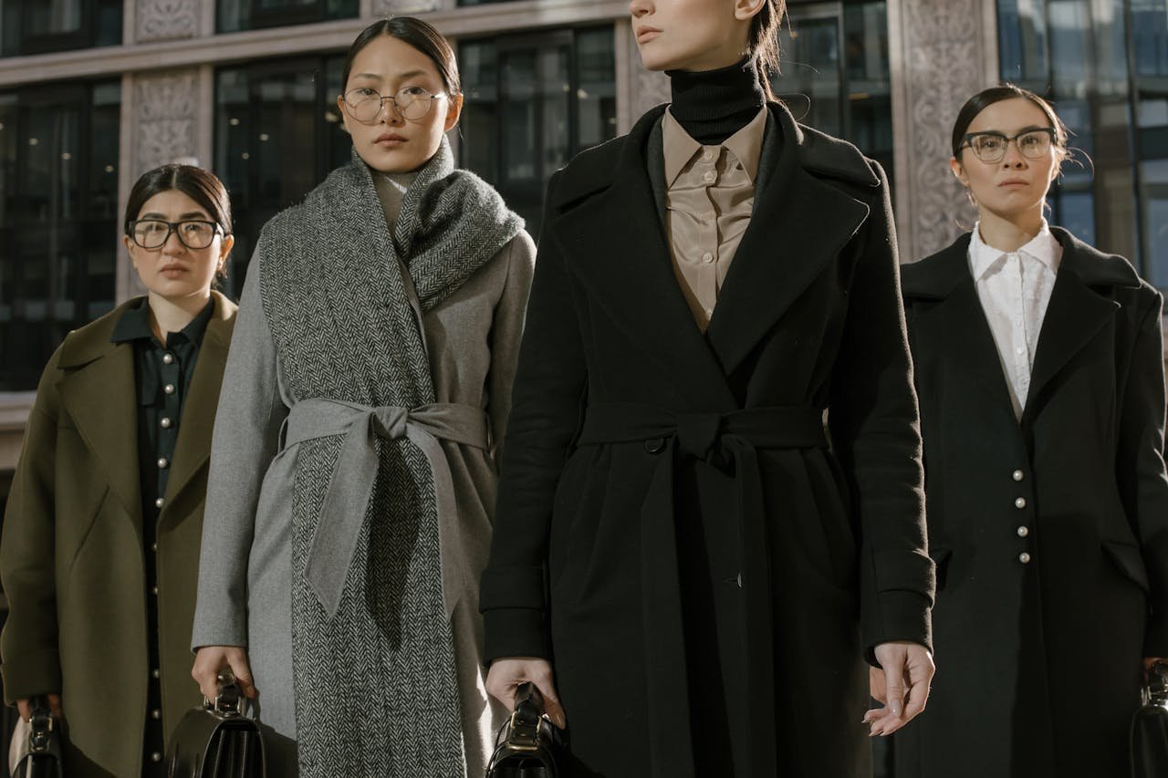 A group of fashionable women in coats standing confidently in an urban environment.